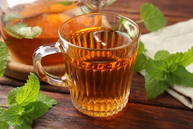 Photo of Aromatic lemon balm tea in glass cup, teapot and fresh leaves on wooden table, closeup