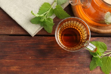 Photo of Aromatic lemon balm tea in glass cup, teapot and fresh leaves on wooden table, flat lay. Space for text