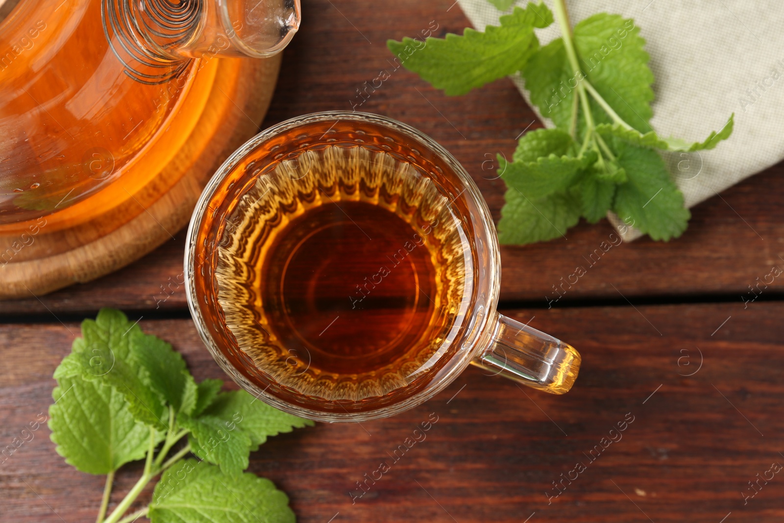 Aromatic lemon balm tea in glass cup, teapot and fresh leaves on wooden table, flat lay Photo of Aromatic lemon balm tea in glass cup, teapot and fresh leaves on wooden table, flat lay