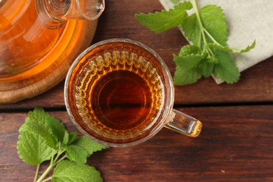Photo of Aromatic lemon balm tea in glass cup, teapot and fresh leaves on wooden table, flat lay