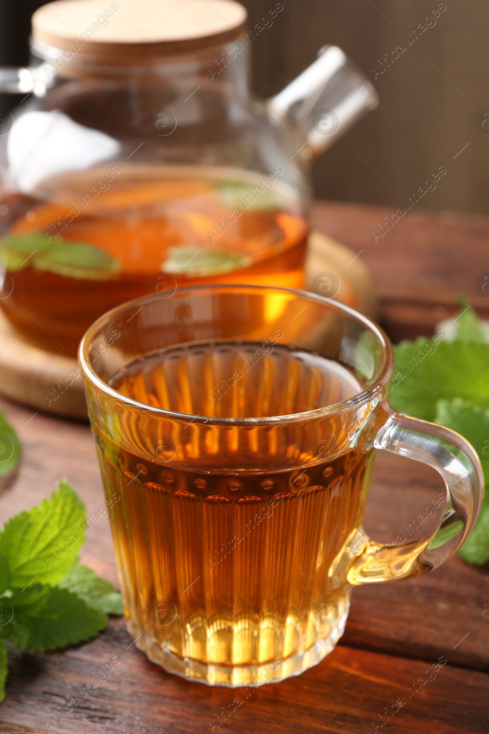 Aromatic lemon balm tea in glass cup, teapot and fresh leaves on wooden table, closeup Photo of Aromatic lemon balm tea in glass cup, teapot and fresh leaves on wooden table, closeup