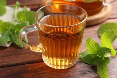 Photo of Aromatic lemon balm tea in glass cup and fresh leaves on wooden table, closeup