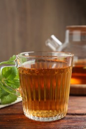 Photo of Aromatic lemon balm tea in glass cup, teapot and fresh leaves on wooden table, closeup
