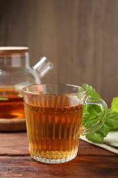 Photo of Aromatic lemon balm tea in glass cup, teapot and fresh leaves on wooden table
