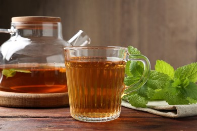 Photo of Aromatic lemon balm tea in glass cup, teapot and fresh leaves on wooden table