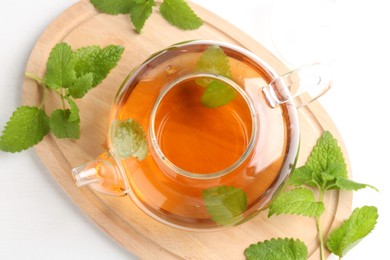 Photo of Aromatic lemon balm tea in glass teapot and fresh leaves on white table, top view