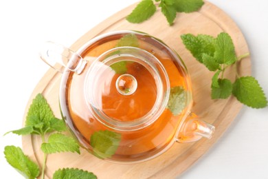 Photo of Aromatic lemon balm tea in glass teapot and fresh leaves on white table, top view