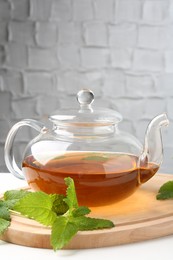 Photo of Aromatic lemon balm tea in glass teapot and fresh leaves on white table against light background
