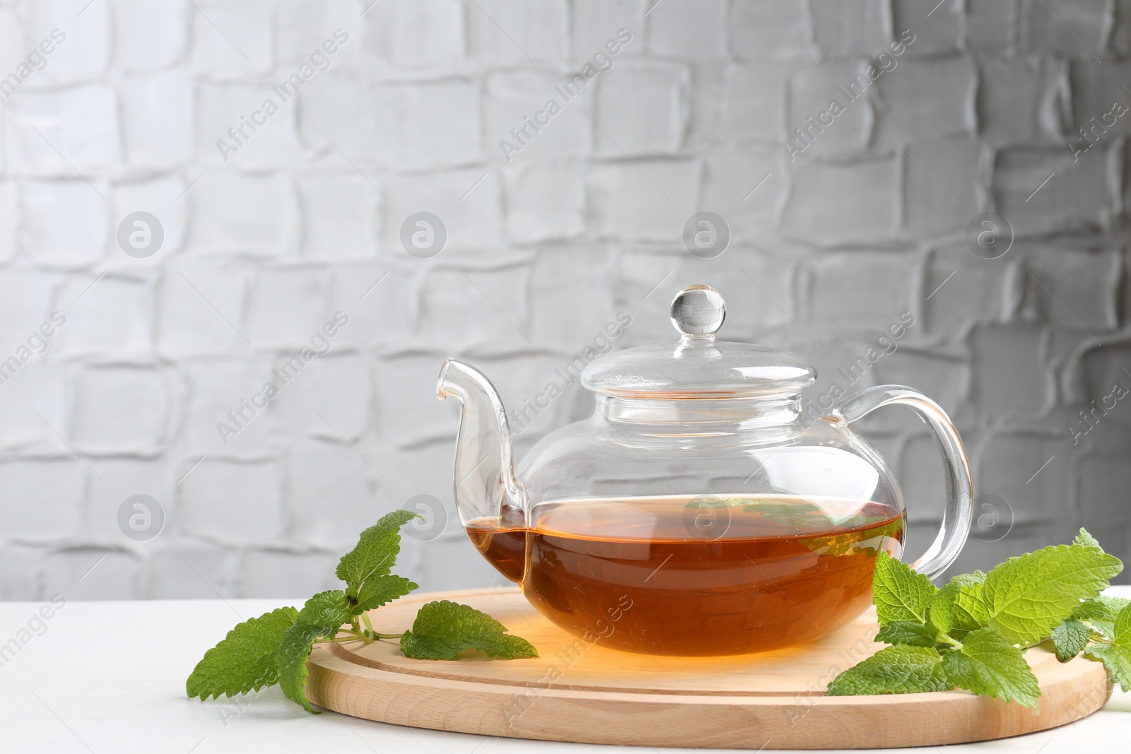 Aromatic lemon balm tea in glass teapot and fresh leaves on white table against light background, space for text Photo of Aromatic lemon balm tea in glass teapot and fresh leaves on white table against light background, space for text