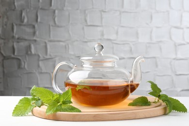 Photo of Aromatic lemon balm tea in glass teapot and fresh leaves on white table against light background