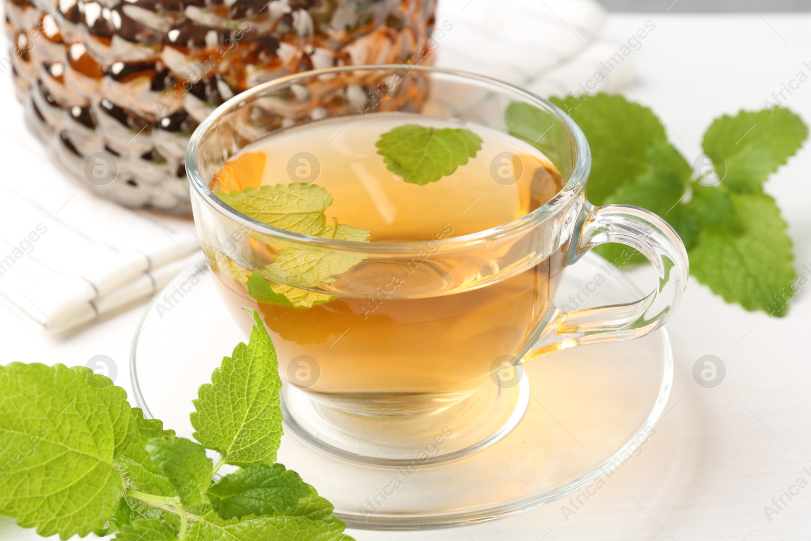 Aromatic lemon balm tea in glass cup, teapot and fresh leaves on white table, closeup Photo of Aromatic lemon balm tea in glass cup, teapot and fresh leaves on white table, closeup