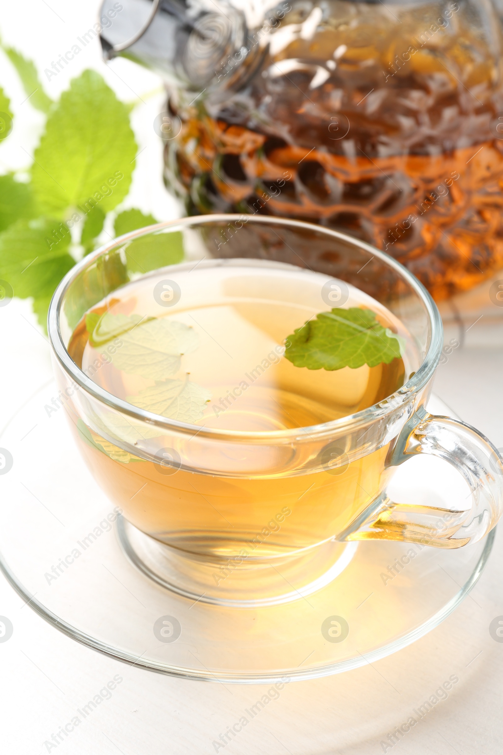Aromatic lemon balm tea in glass cup, teapot and fresh leaves on white table, closeup Photo of Aromatic lemon balm tea in glass cup, teapot and fresh leaves on white table, closeup