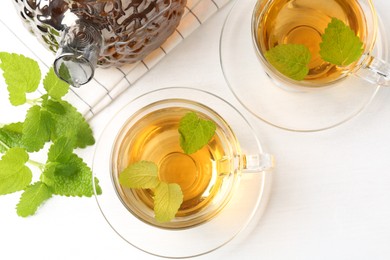 Photo of Aromatic lemon balm tea in glass cups, teapot and fresh leaves on white table, flat lay