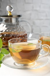 Photo of Aromatic lemon balm tea in glass cups, teapot and fresh leaves on white table, closeup