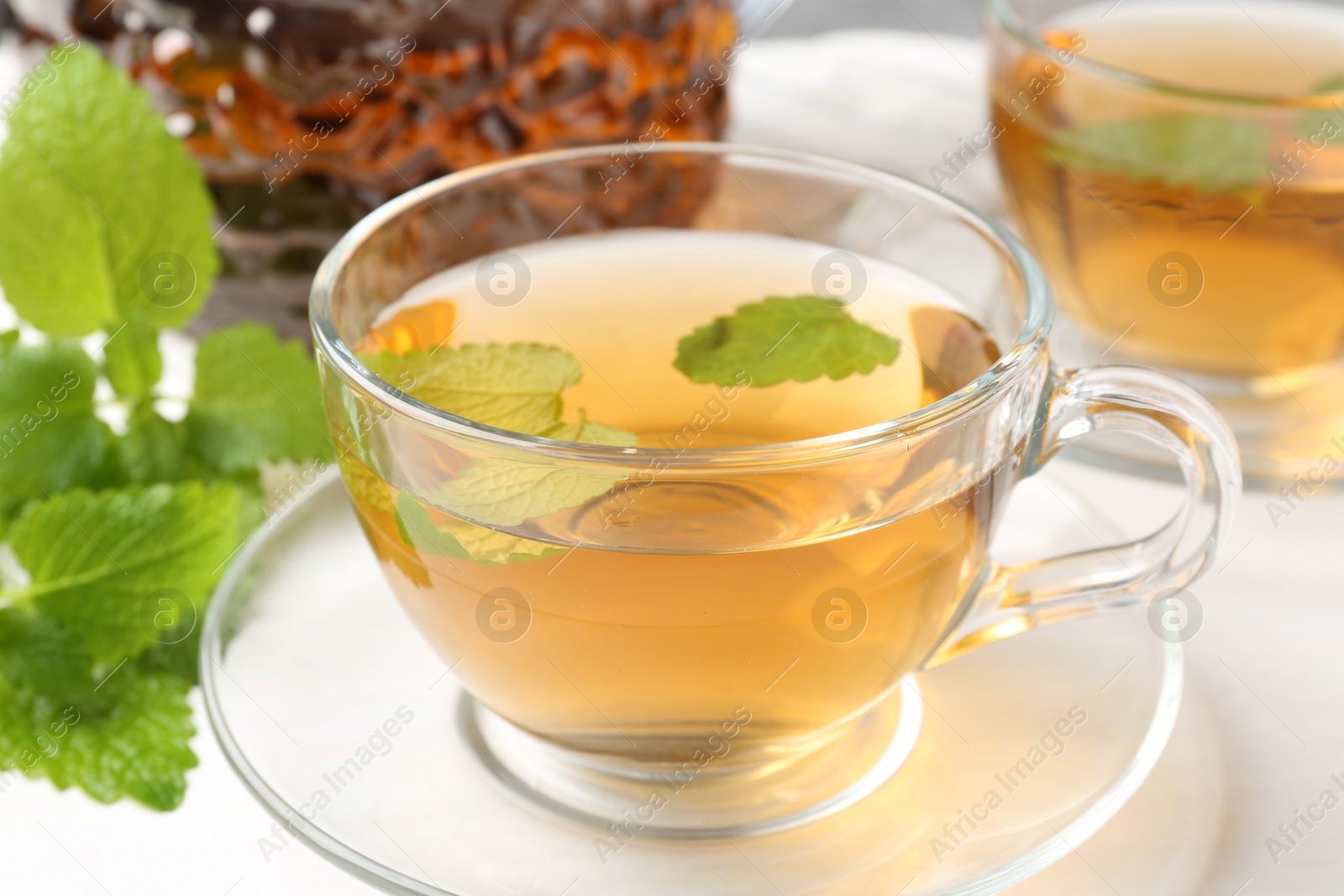 Aromatic lemon balm tea in glass cups, teapot and fresh leaves on white table, closeup Photo of Aromatic lemon balm tea in glass cups, teapot and fresh leaves on white table, closeup