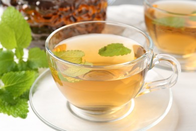 Photo of Aromatic lemon balm tea in glass cups, teapot and fresh leaves on white table, closeup