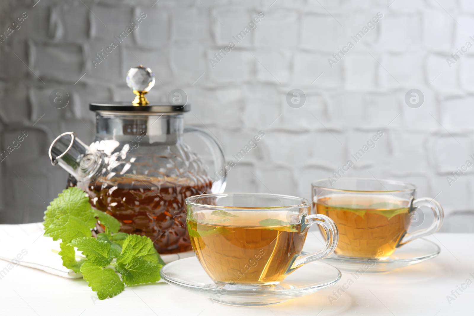 Aromatic lemon balm tea in glass cups, teapot and fresh leaves on white table Photo of Aromatic lemon balm tea in glass cups, teapot and fresh leaves on white table