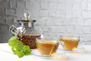 Photo of Aromatic lemon balm tea in glass cups, teapot and fresh leaves on white table
