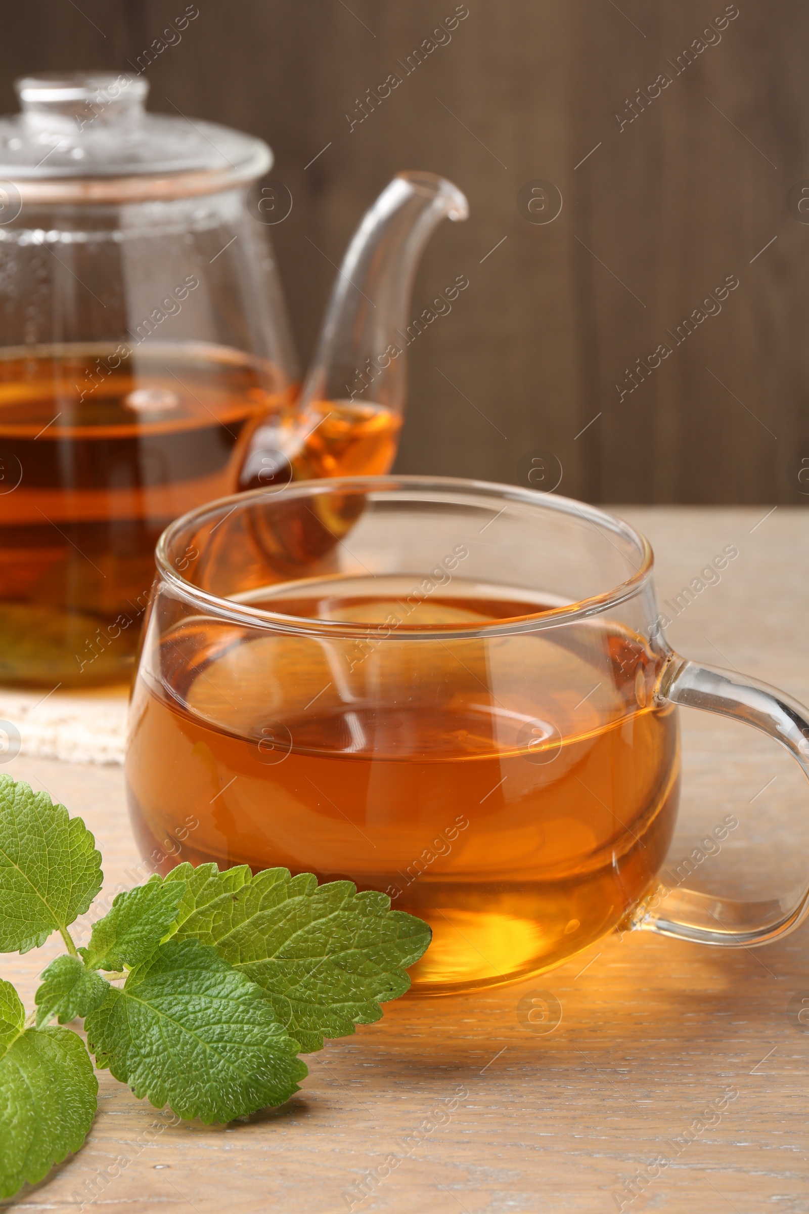 Aromatic lemon balm tea in glass cup, teapot and fresh leaves on wooden table, closeup Photo of Aromatic lemon balm tea in glass cup, teapot and fresh leaves on wooden table, closeup