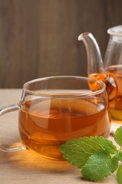 Photo of Aromatic lemon balm tea in glass cup, teapot and fresh leaves on wooden table, closeup
