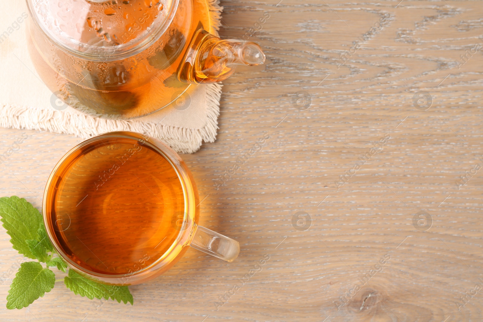 Aromatic lemon balm tea in glass cup, teapot and fresh leaves on wooden table, flat lay. Space for text Photo of Aromatic lemon balm tea in glass cup, teapot and fresh leaves on wooden table, flat lay. Space for text