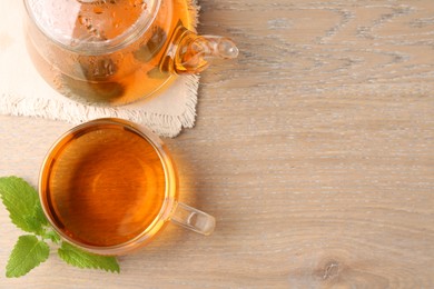 Photo of Aromatic lemon balm tea in glass cup, teapot and fresh leaves on wooden table, flat lay. Space for text