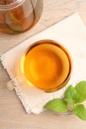 Photo of Aromatic lemon balm tea in glass cup, teapot and fresh leaves on wooden table, flat lay