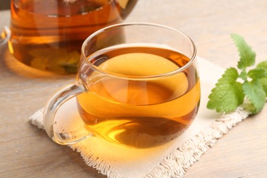 Photo of Aromatic lemon balm tea in glass cup, teapot and fresh leaves on wooden table, closeup