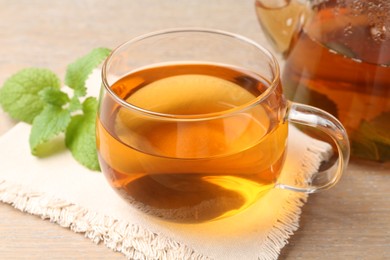 Photo of Aromatic lemon balm tea in glass cup, teapot and fresh leaves on wooden table, closeup