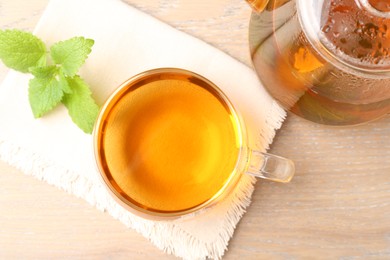 Photo of Aromatic lemon balm tea in glass cup, teapot and fresh leaves on wooden table, flat lay
