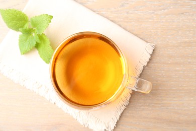Photo of Aromatic lemon balm tea in glass cup and fresh leaves on wooden table, flat lay