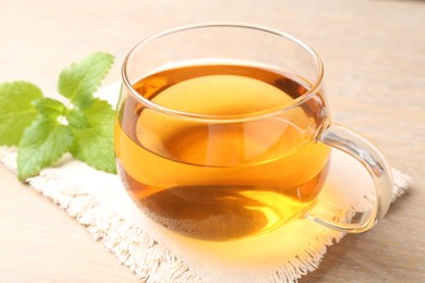 Photo of Aromatic lemon balm tea in glass cup and fresh leaves on table, closeup