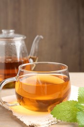 Photo of Aromatic lemon balm tea in glass cup, teapot and fresh leaves on table, closeup
