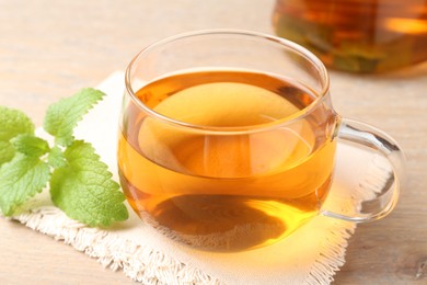 Photo of Aromatic lemon balm tea in glass cup and fresh leaves on table, closeup