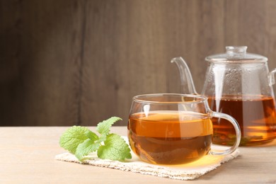 Photo of Aromatic lemon balm tea in glass cup, teapot and fresh leaves on wooden table, space for text
