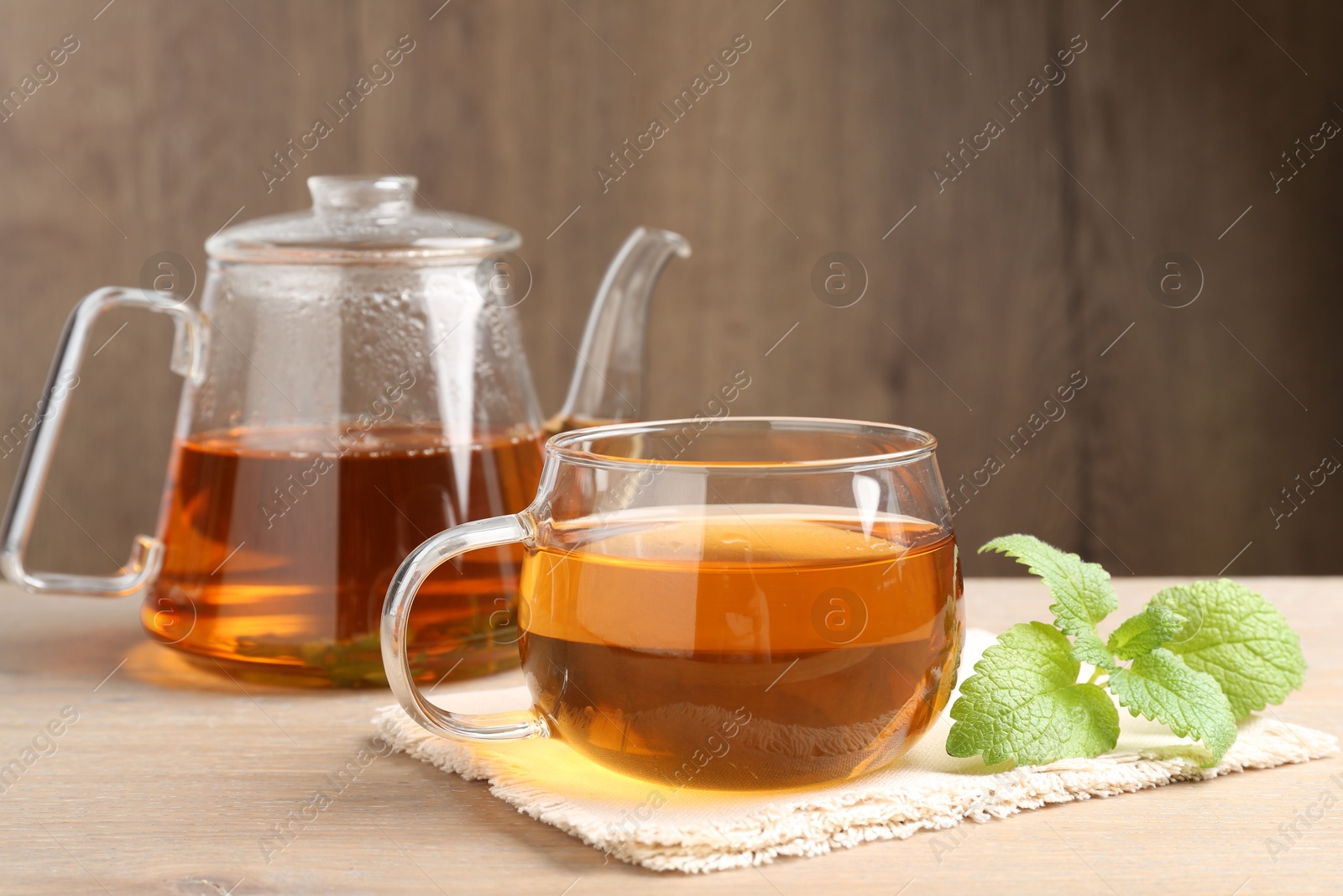 Aromatic lemon balm tea in glass cup, teapot and fresh leaves on wooden table Photo of Aromatic lemon balm tea in glass cup, teapot and fresh leaves on wooden table