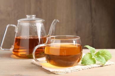 Photo of Aromatic lemon balm tea in glass cup, teapot and fresh leaves on wooden table