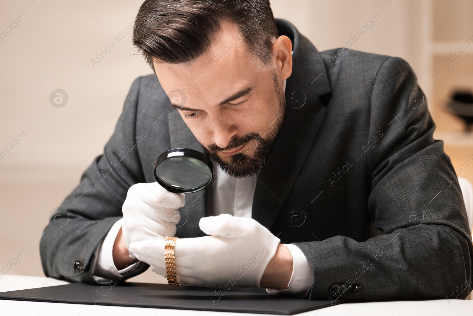 Appraiser evaluating luxury wristwatch at table indoors Photo of Appraiser evaluating luxury wristwatch at table indoors