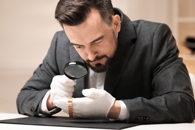 Photo of Appraiser evaluating luxury wristwatch at table indoors