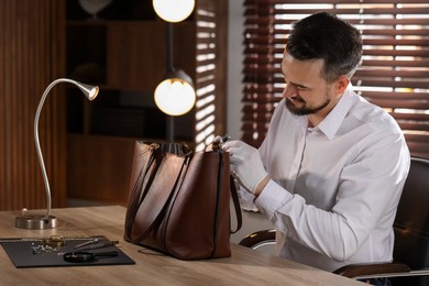 Photo of Appraiser with loupe evaluating leather bag at table indoors