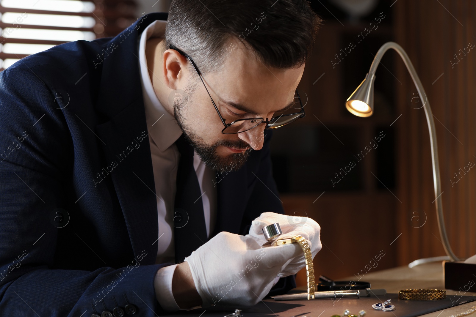 Appraiser with loupe evaluating luxury wristwatch at table indoors Photo of Appraiser with loupe evaluating luxury wristwatch at table indoors