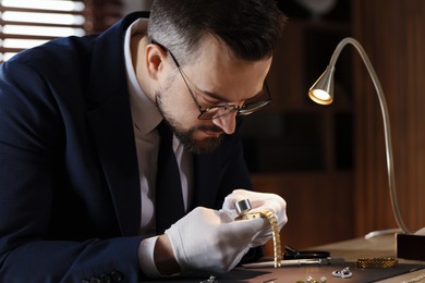 Photo of Appraiser with loupe evaluating luxury wristwatch at table indoors