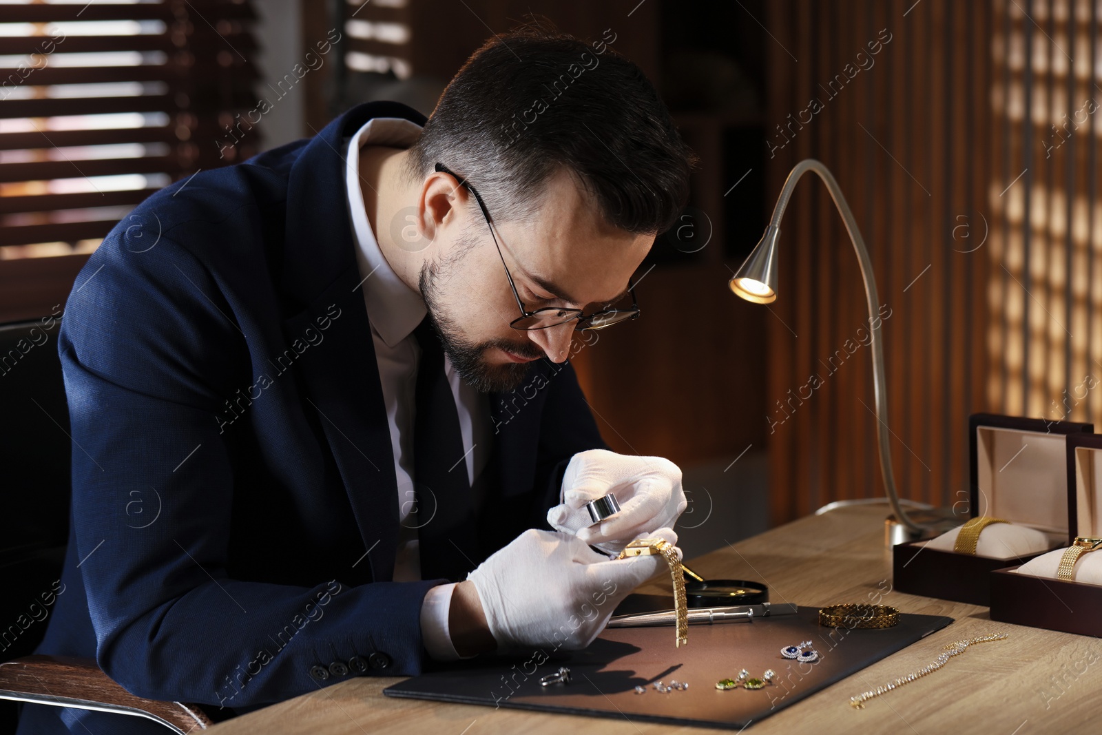 Appraiser with loupe evaluating luxury wristwatch at table indoors Photo of Appraiser with loupe evaluating luxury wristwatch at table indoors