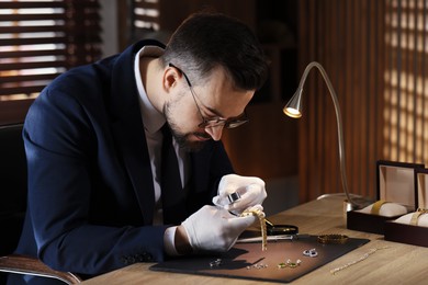 Photo of Appraiser with loupe evaluating luxury wristwatch at table indoors