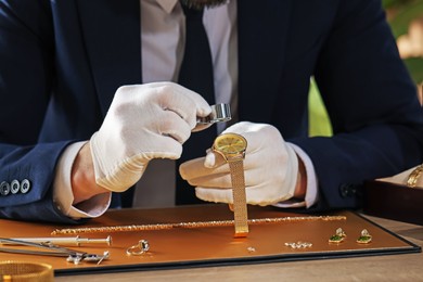Photo of Appraiser with loupe evaluating luxury wristwatch at table indoors, closeup
