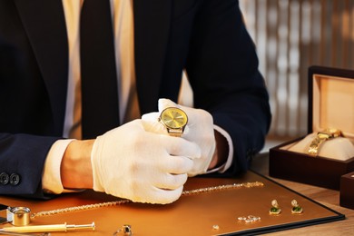 Photo of Appraiser working with luxury wristwatch at table indoors, closeup