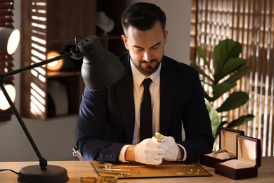 Photo of Appraiser working with luxury wristwatch at table indoors
