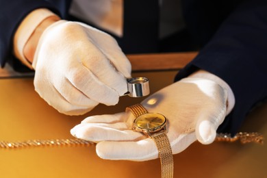 Photo of Appraiser with loupe evaluating luxury wristwatch at table, closeup