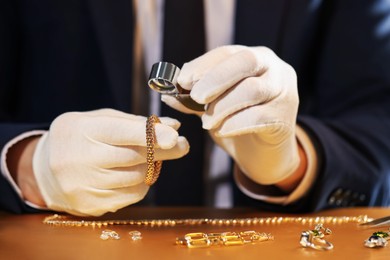 Photo of Appraiser with loupe evaluating luxury jewelry at table, closeup