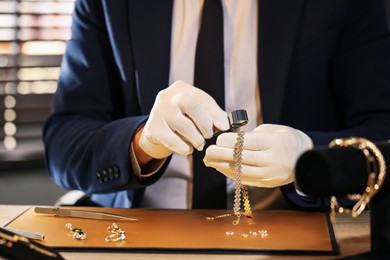 Photo of Appraiser with loupe evaluating luxury jewelry at table, closeup